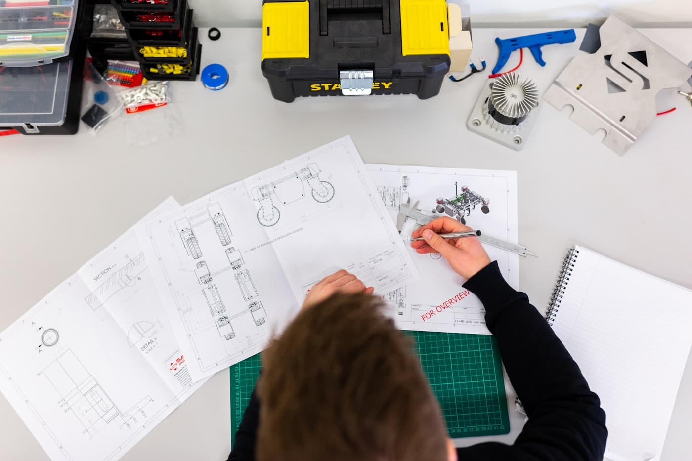 Illustrative overhead view of an engineering workshop, with technical drawings, measuring tools and components on a worktable.